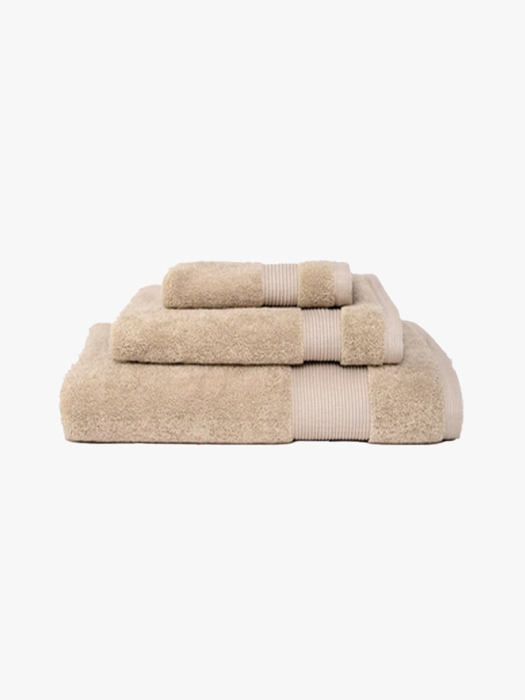 Saatva Plush Towel Collection stack of folded tan towels on light gray background