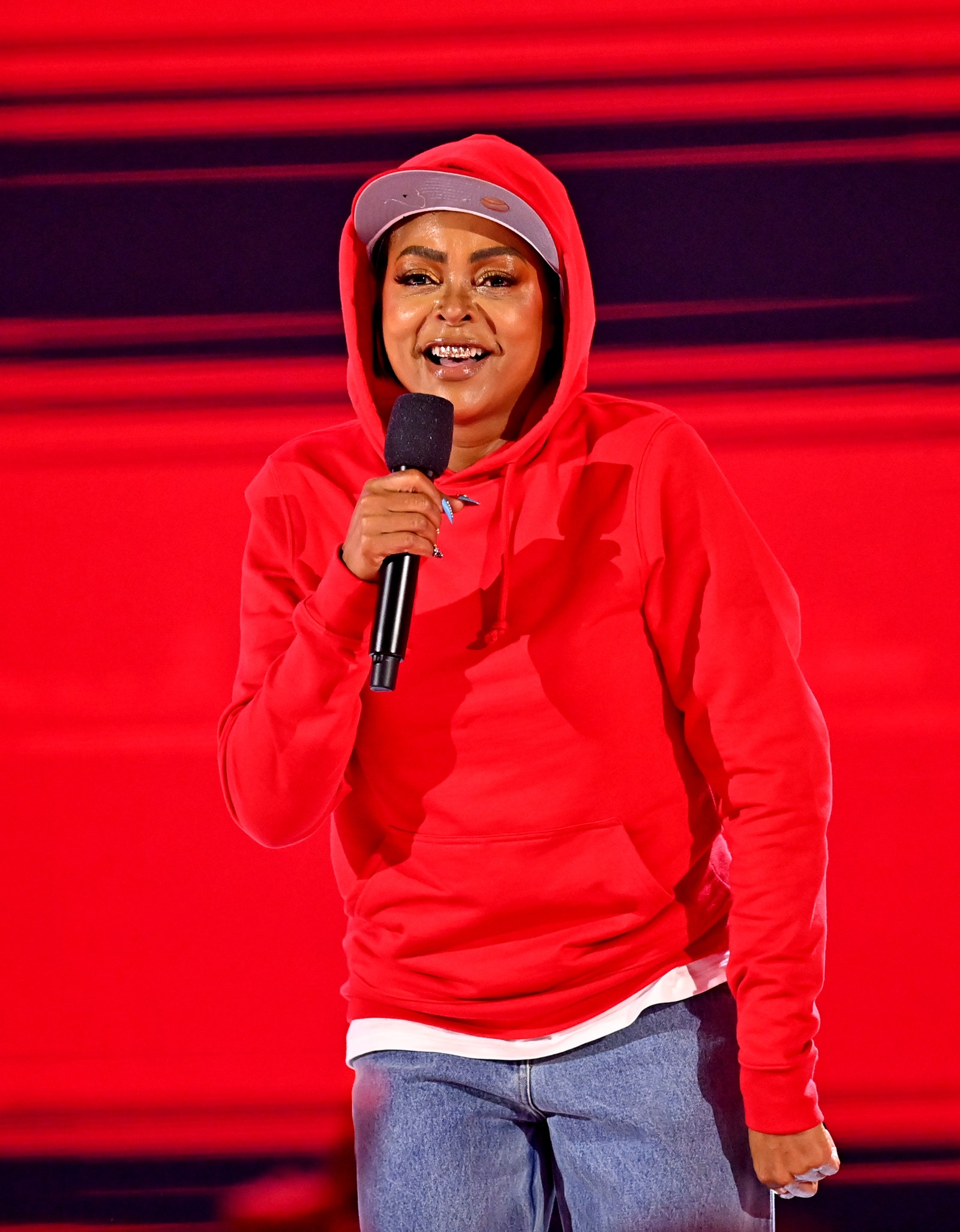Taraji P. Henson wears a red hoodie and hat onstage.