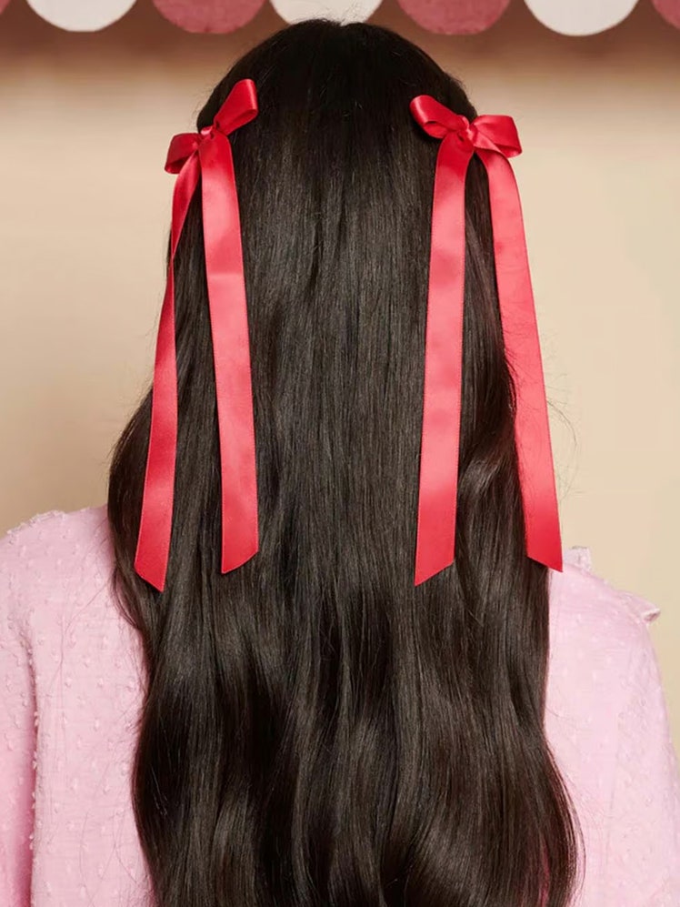 Someone with long brunette hair modeling the Sister Jane Cranberry Hair Bows on a beige background