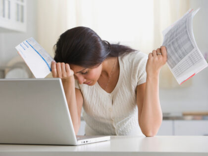 Overwhelmed woman holding bills in front of laptop - stock photo