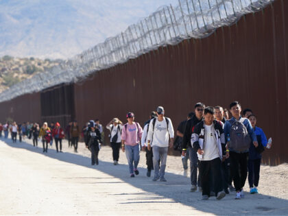 A group of people, including many from China, walk along the wall after crossing the borde