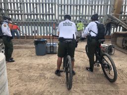 Border Patrol officials cycle by the barriers and watch as the crews pour in concrete. The wall is not funded by the government.