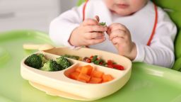 Little baby eating food in high chair, closeup