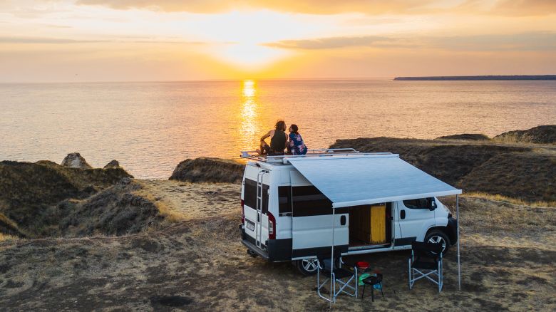 Aerial view of the heterosexual couple on the roof of camper van on seaside  at sunset