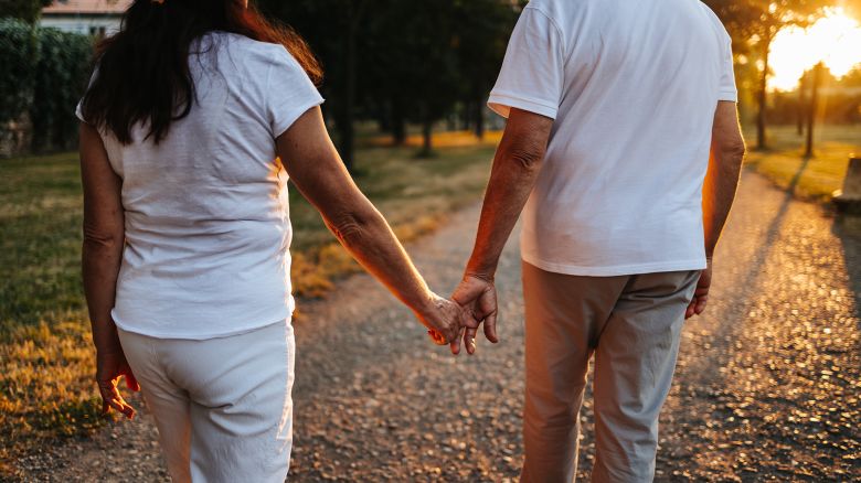 Cheerful senior couple walking in public park at sunset. They enjoy a beautiful day in beautiful nature and spread positive energy and love