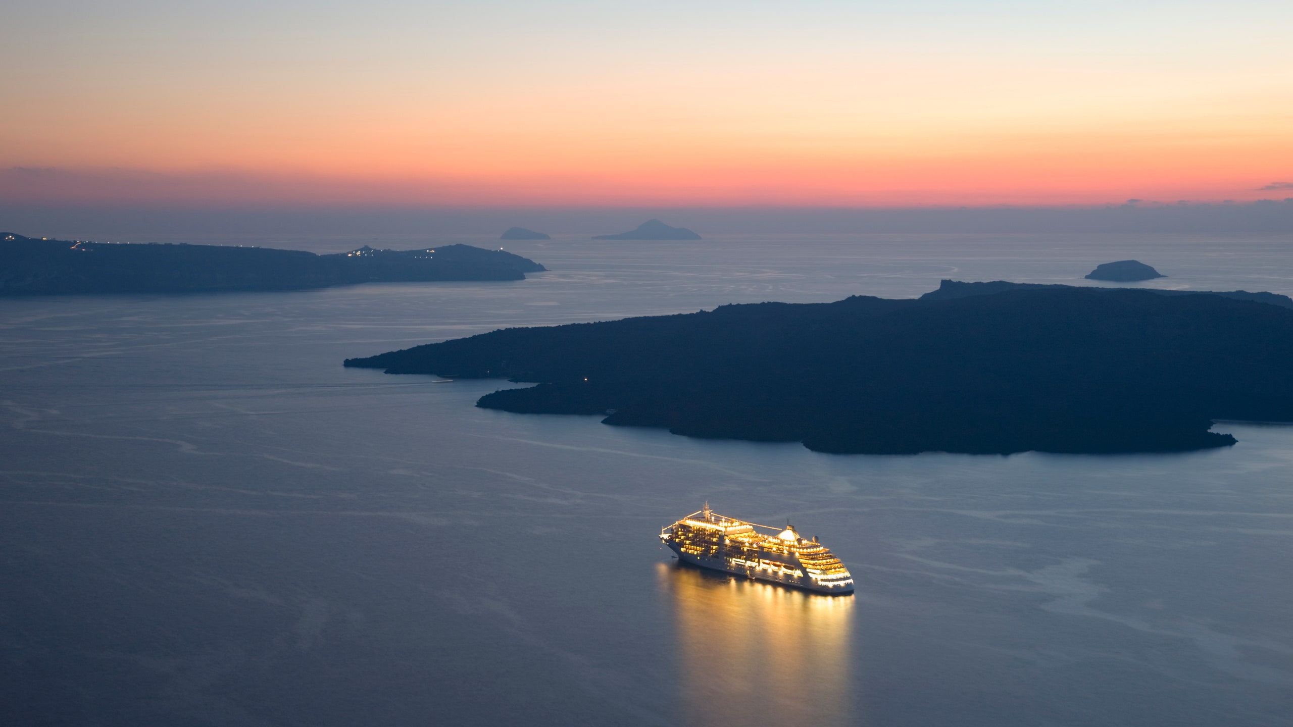 View from clifftop over the caldera after sunset illuminated cruise ship anchored off the volcanic island of Nea Kameni...