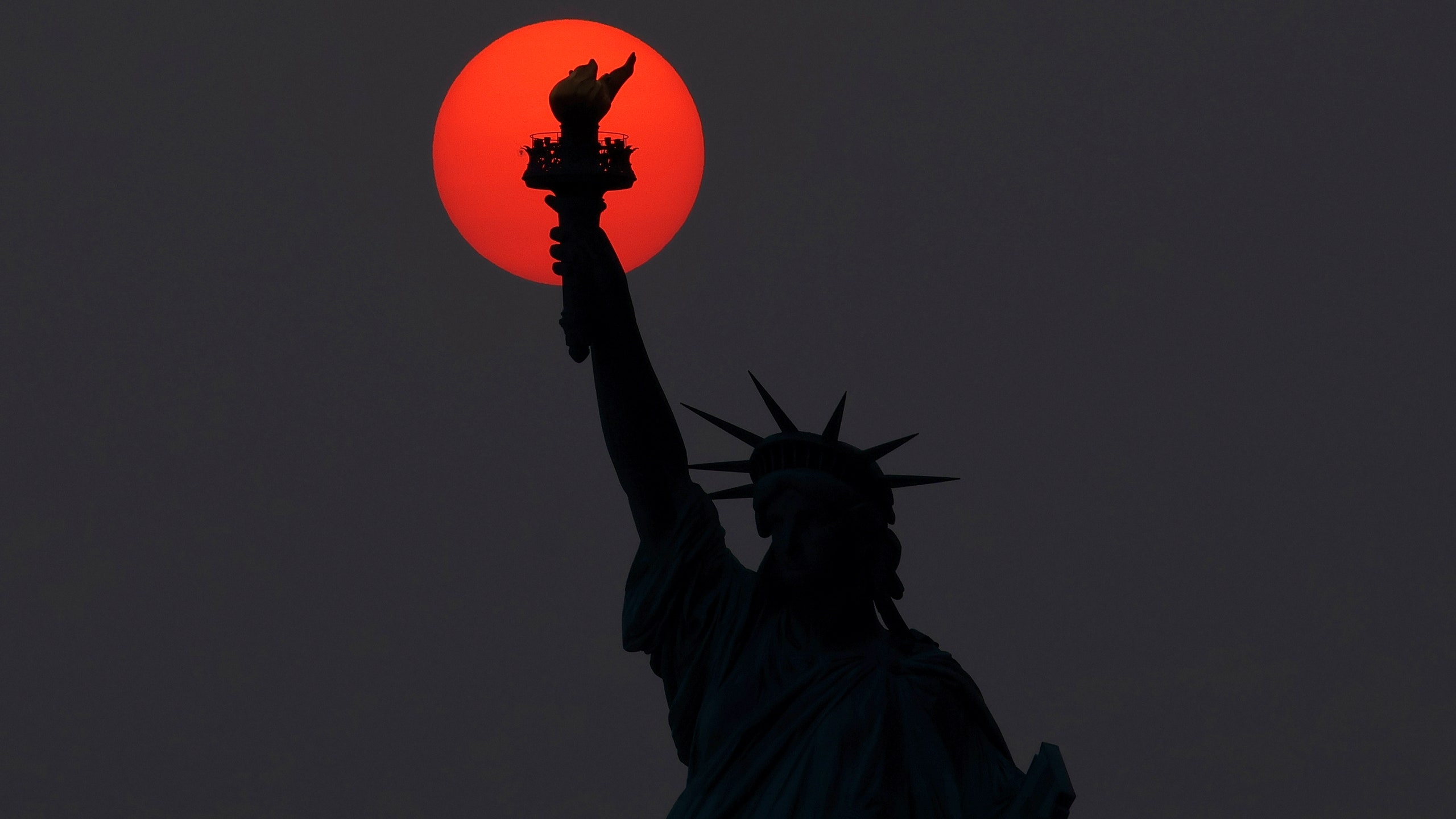 The sun sets behind the Statue of Liberty.