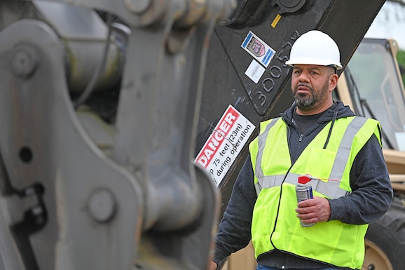 A man in safety gear looks at a excavator grapple.