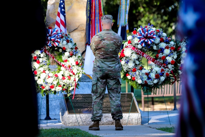 A soldier stands with back to the camera between two large wreaths.