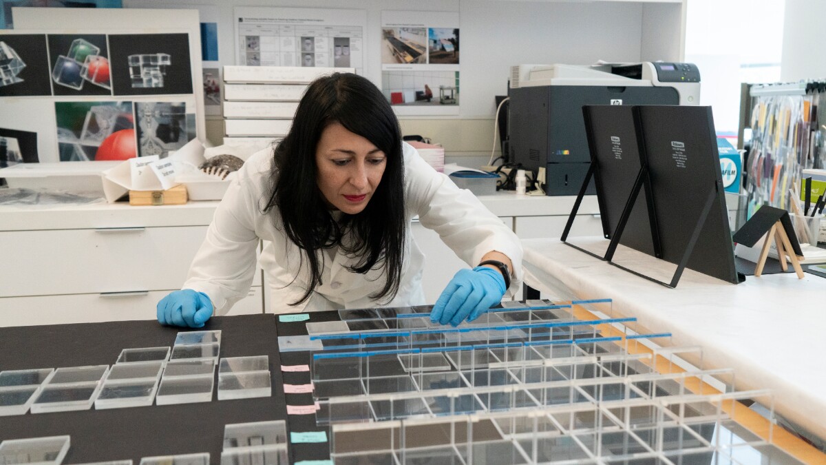 A scientist in a lab coat inspects several clear plastic samples arrayed in front of her on a table.