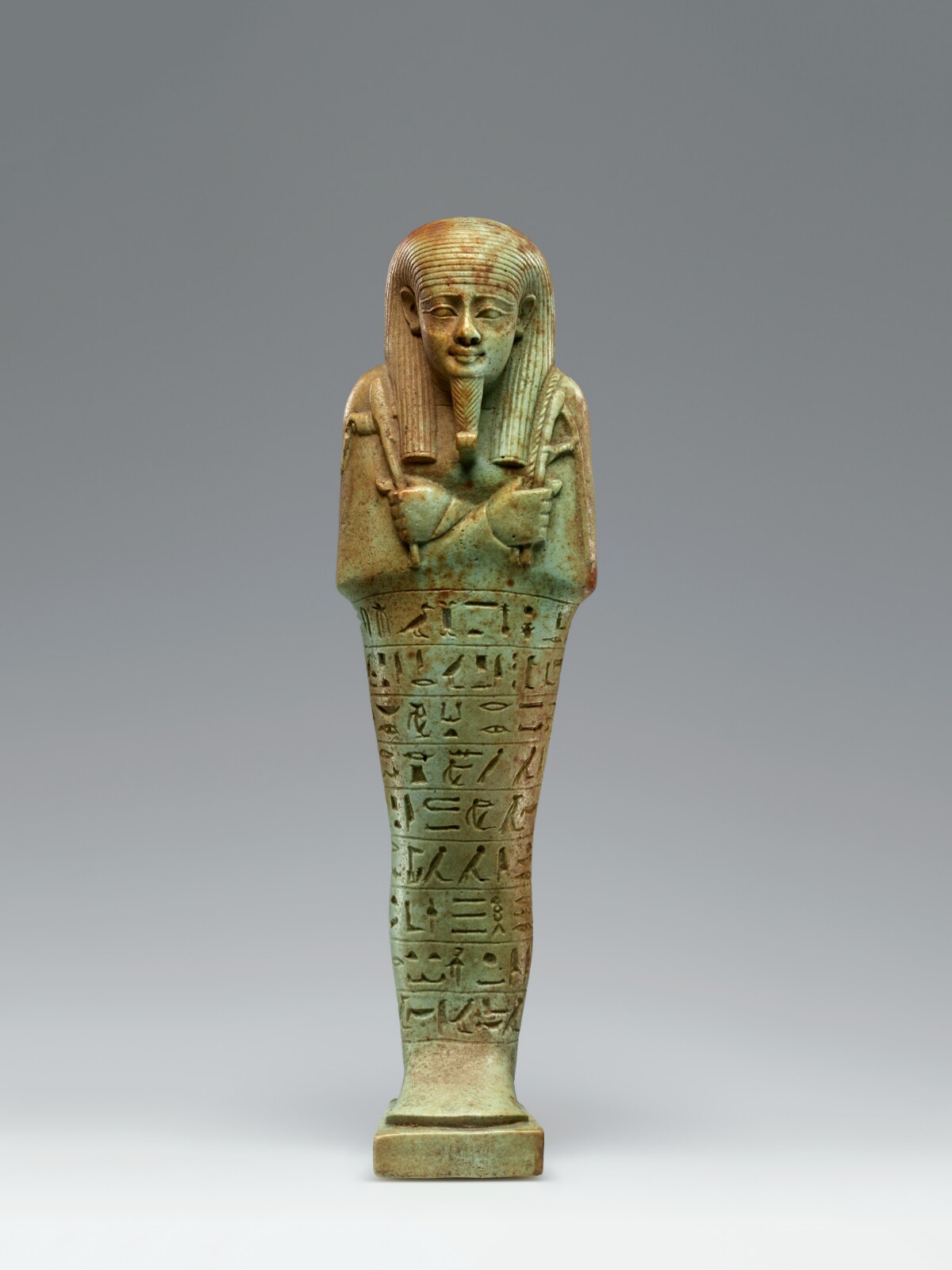 Golden-green statue stands with arms crossed and hieroglyphs on its body.