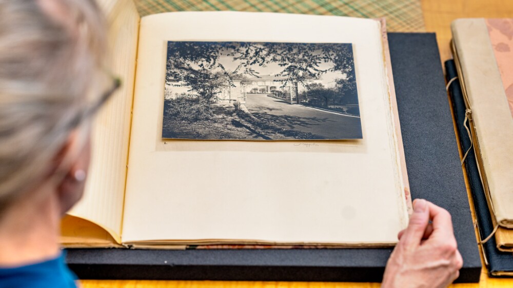 A person sits in a glass room in a library looking through old photo albums.