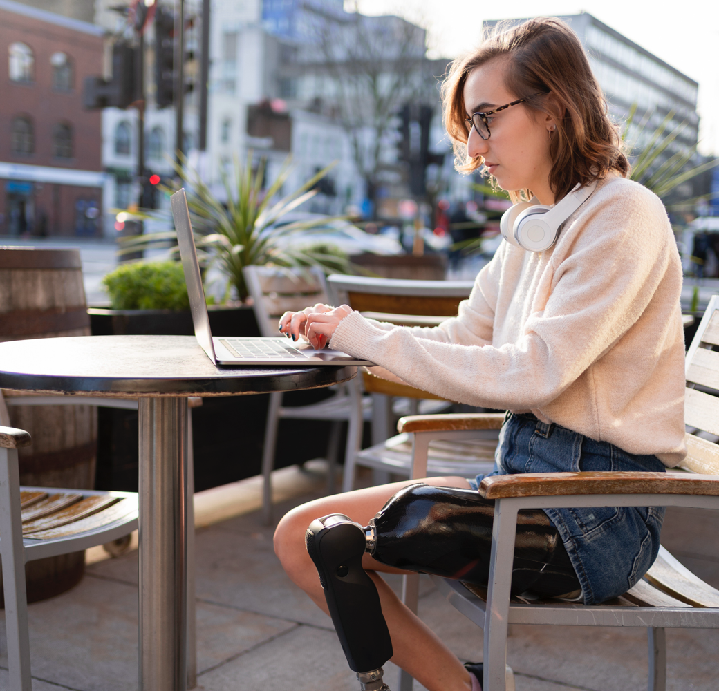 Woman with prosthetic leg sitting at table working on laptop