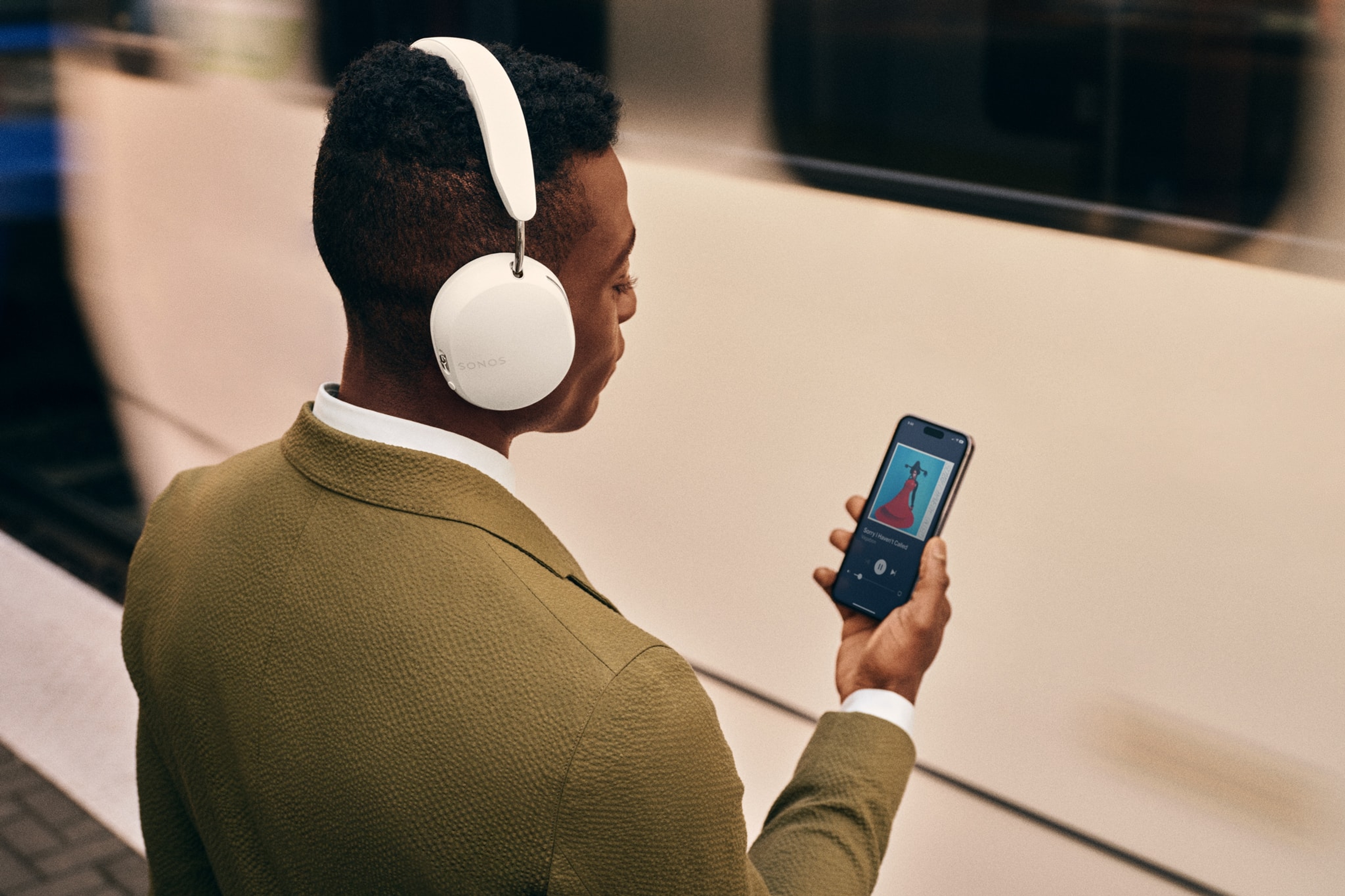 Train commuter using white Sonos Ace headphones at a train station