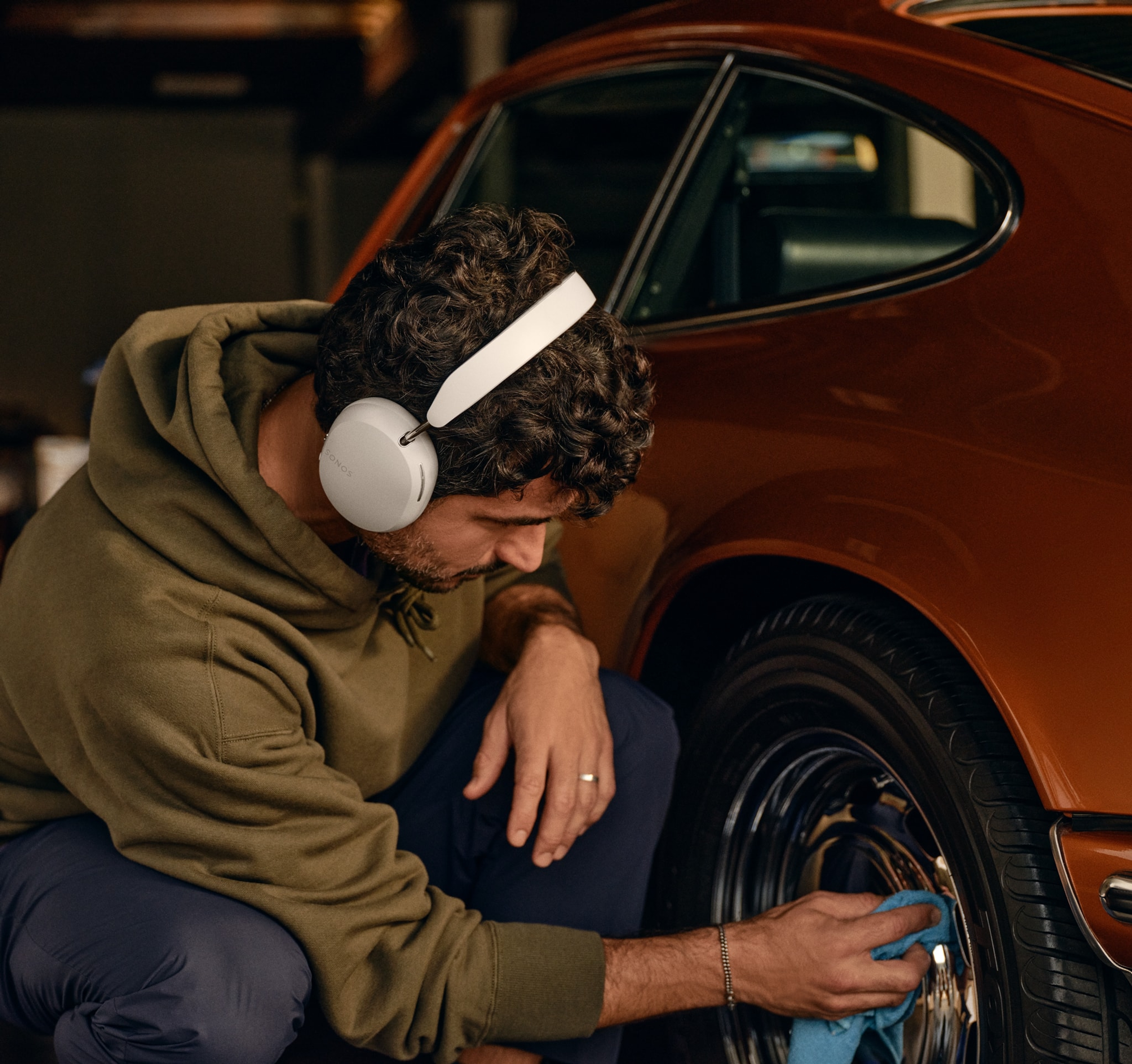 Male user wearing a pair of soft white Sonos Ace headphones while polishing wheels of a classic car