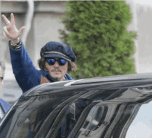 a man wearing sunglasses and a hat is waving from a car window