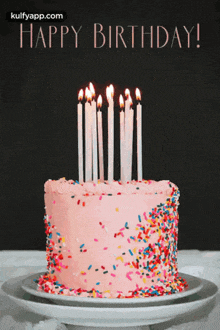 a pink birthday cake with candles and sprinkles and the words happy birthday