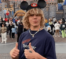 a young man wearing a mickey mouse ear hat is giving a thumbs up .