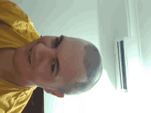 a man with a shaved head and a yellow shirt is smiling