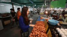 a woman stands in front of a display of eggs with a sign that says ' eggs ' on it