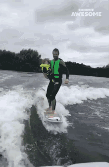 a man in a wet suit is carrying a child on a surfboard with the words " awesome " written above him