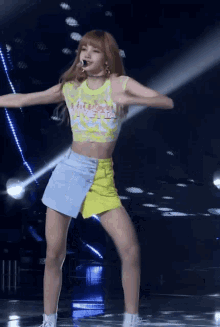 a woman wearing a yellow top and a blue skirt is dancing on stage