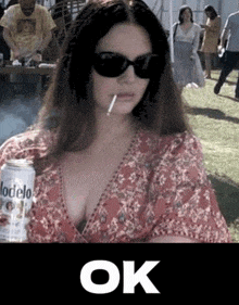 a woman wearing sunglasses is smoking a cigarette and holding a can of modelo beer