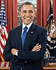 barack obama is standing in front of a desk with his arms crossed and smiling .