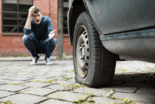 a man is squatting down in front of a car with a flat tire