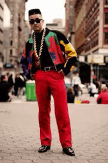 a man in a colorful jacket and red pants is standing on a city street .