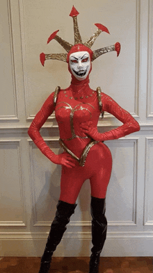 a woman in a red costume with a white face is standing in front of a white wall