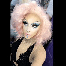 a drag queen with pink hair is wearing a black top