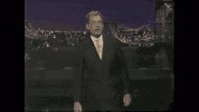 a man in a suit and tie is standing on a stage in front of a bridge .