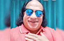 a bald man wearing a red shirt and blue sunglasses is smiling .