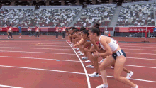 a group of female athletes are lined up on a track with tokyo 2020 written on the wall behind them