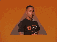 a man wearing a black t-shirt with chinese writing on it is standing in front of an orange background .