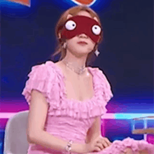 a woman in a pink dress is sitting in a chair wearing a mask on her eyes .