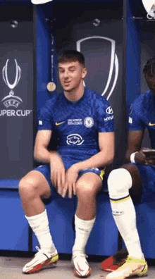 a soccer player is sitting on a bench in a locker room in front of a uefa super cup sign