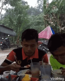 a man sitting at a table eating food with a pink and blue tent in the background and the words viralhog on the bottom