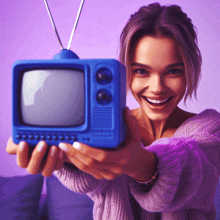 a woman in a purple sweater is smiling and holding a small blue television