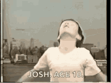 a young girl is standing in front of a city skyline with her arms outstretched and says `` josh age 10 '' .