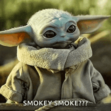 a baby yoda from the mandalorian is sitting on a wooden fence and smoking a cigarette .