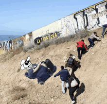 a group of people are climbing up a hill near a wall that has la frontera written on it