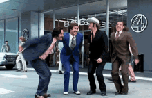 a group of men in suits and ties are dancing on the sidewalk in front of a building with the number four on it .