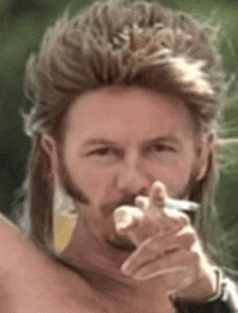 a man with a mullet is smoking a cigarette and pointing at the camera .