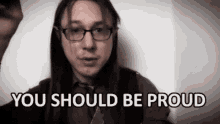 a man with long hair wearing glasses and a tie says you should be proud .