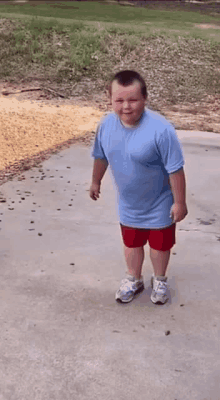 a young boy wearing a blue shirt and red shorts is standing on a sidewalk