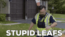 a man wearing a safety vest is raking leaves in front of a garage with the words stupid leaves written above him