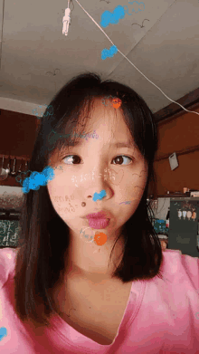 a girl in a pink shirt has drawings on her face including one that says ' a ' on it