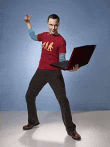 a man wearing a red shirt that says ' a.k. ' on it is holding a red laptop